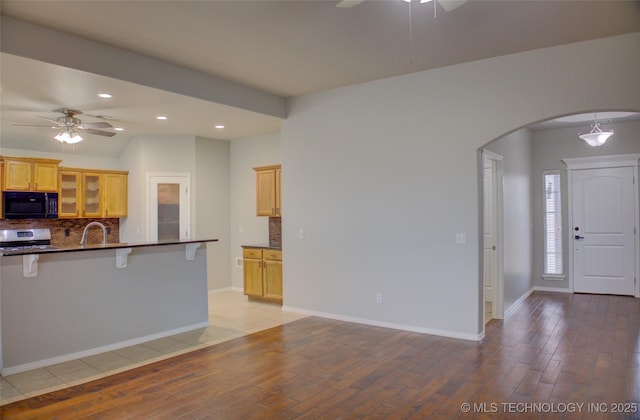 kitchen featuring arched walkways, decorative backsplash, dark countertops, stainless steel range with electric stovetop, and black microwave