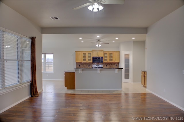 kitchen featuring tasteful backsplash, visible vents, light wood-style flooring, glass insert cabinets, and black microwave