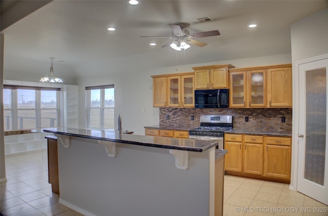 kitchen featuring stainless steel gas stove, visible vents, decorative backsplash, a breakfast bar area, and black microwave