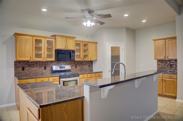 kitchen featuring stainless steel range with gas cooktop, a center island with sink, light tile patterned floors, a sink, and black microwave