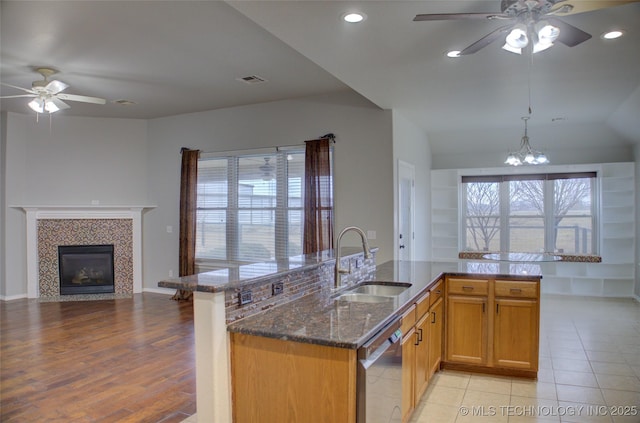 kitchen with a tiled fireplace, open floor plan, a sink, dark stone counters, and dishwasher