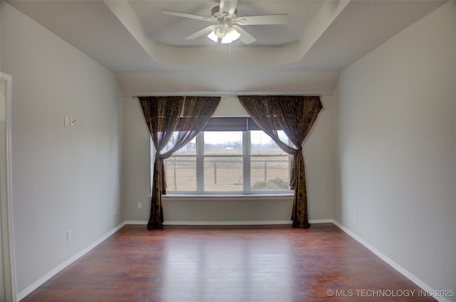 unfurnished room with a ceiling fan, a tray ceiling, baseboards, and wood finished floors