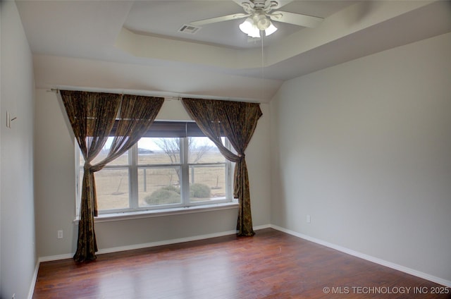 spare room with wood finished floors, a raised ceiling, visible vents, and baseboards