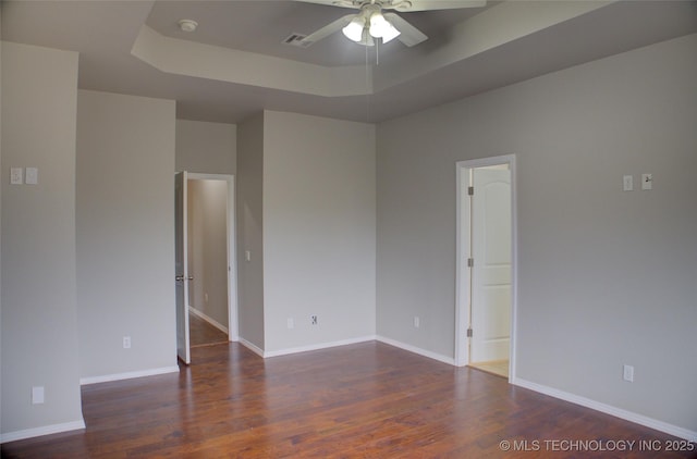 spare room featuring baseboards, visible vents, ceiling fan, wood finished floors, and a tray ceiling