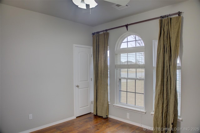 unfurnished room with dark wood-style floors, visible vents, and baseboards