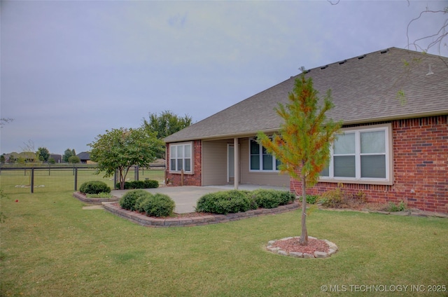 ranch-style house with a patio, brick siding, a front yard, and a shingled roof