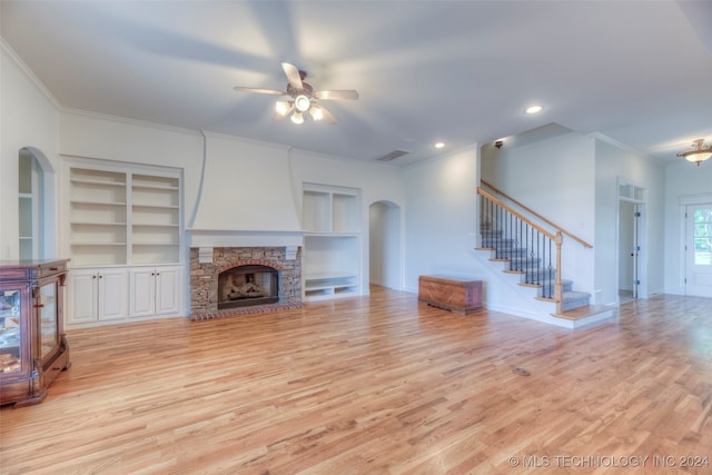 unfurnished living room with a stone fireplace, ornamental molding, built in features, light hardwood / wood-style floors, and ceiling fan