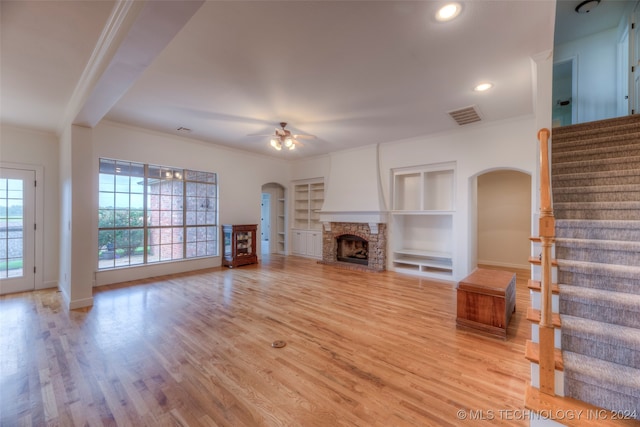 unfurnished living room with ornamental molding, a fireplace, built in shelves, light hardwood / wood-style floors, and ceiling fan