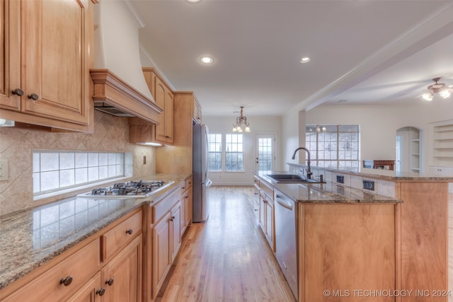 kitchen with custom range hood, decorative backsplash, an island with sink, and sink