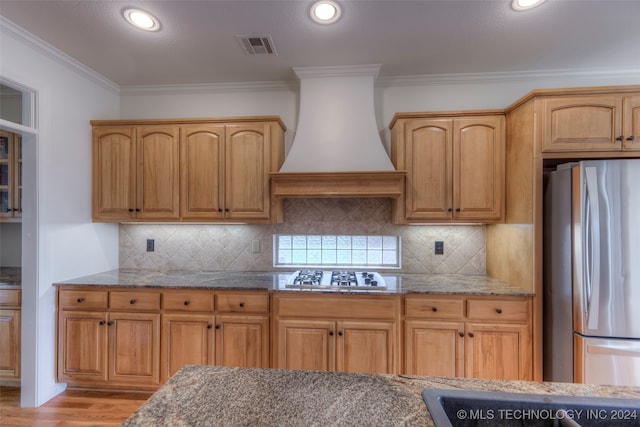 kitchen featuring backsplash, light wood-type flooring, appliances with stainless steel finishes, custom exhaust hood, and light stone counters