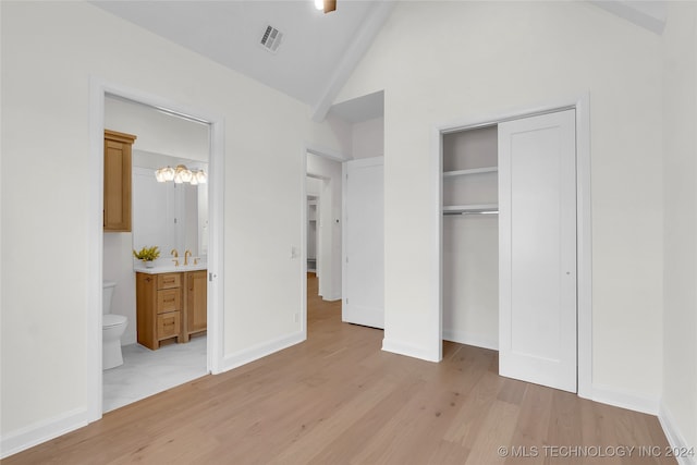 unfurnished bedroom with light wood-type flooring, a closet, vaulted ceiling, ensuite bath, and sink