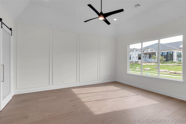 unfurnished room featuring light wood-type flooring, a barn door, ceiling fan, and high vaulted ceiling