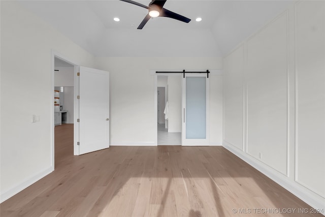 unfurnished bedroom featuring ceiling fan, vaulted ceiling, light hardwood / wood-style floors, and a barn door