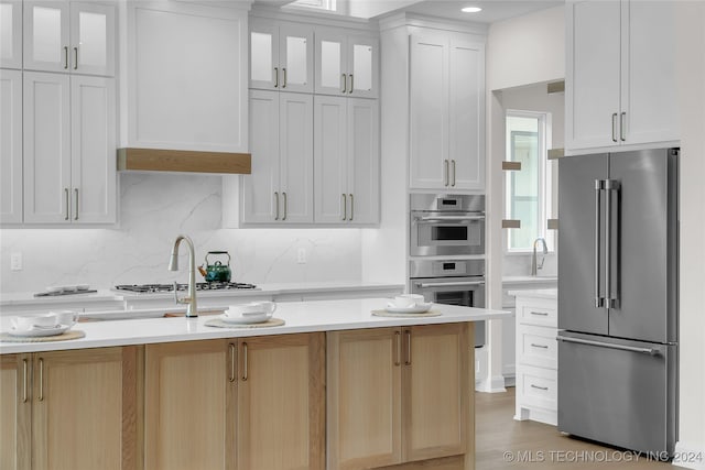 kitchen with light wood-type flooring, backsplash, light brown cabinetry, white cabinets, and stainless steel appliances