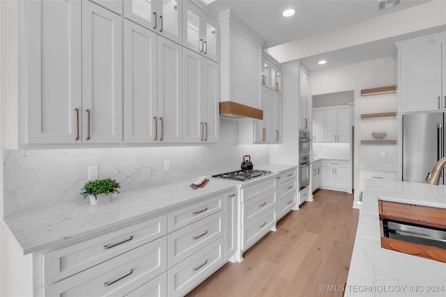 kitchen with stainless steel appliances, light hardwood / wood-style floors, decorative backsplash, white cabinetry, and light stone counters