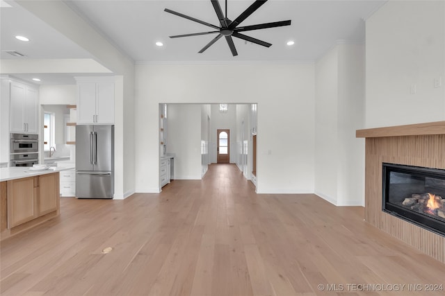 unfurnished living room with ceiling fan, sink, light hardwood / wood-style floors, and ornamental molding