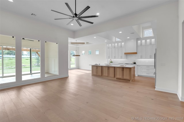 unfurnished living room featuring light wood-type flooring, sink, a towering ceiling, and ceiling fan