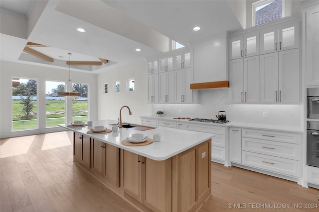 kitchen with an island with sink, white cabinetry, light hardwood / wood-style floors, sink, and decorative light fixtures