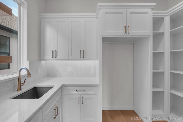 kitchen featuring backsplash, sink, light hardwood / wood-style flooring, light stone countertops, and white cabinets