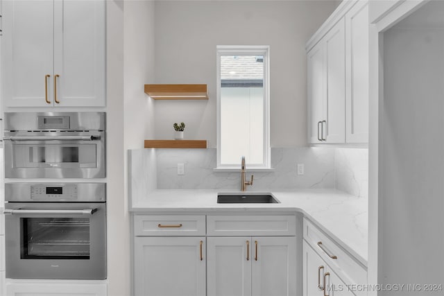 kitchen featuring sink, double oven, decorative backsplash, light stone counters, and white cabinets