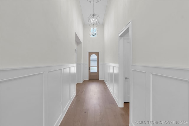 doorway with light wood-type flooring, a towering ceiling, and an inviting chandelier