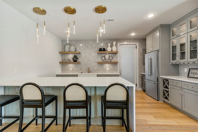 kitchen featuring backsplash, light hardwood / wood-style floors, high end fridge, a kitchen breakfast bar, and gray cabinets