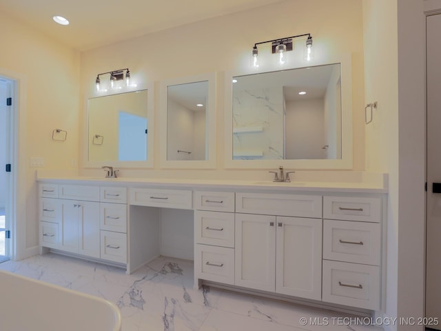 bathroom with double vanity, marble finish floor, a freestanding tub, and a sink