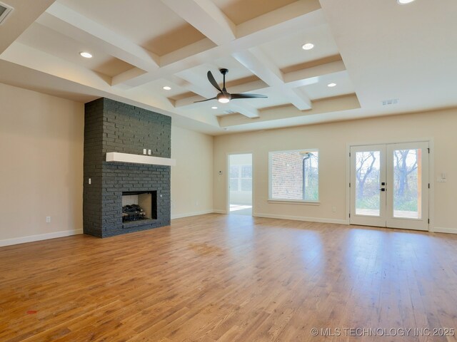 unfurnished living room featuring french doors, coffered ceiling, a brick fireplace, light hardwood / wood-style flooring, and beamed ceiling