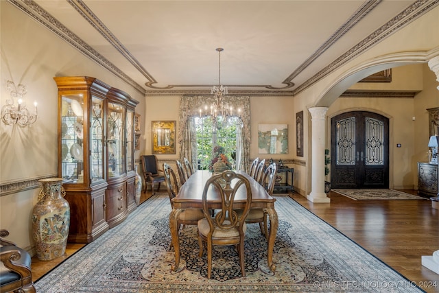 dining room with hardwood / wood-style floors, ornamental molding, an inviting chandelier, french doors, and ornate columns