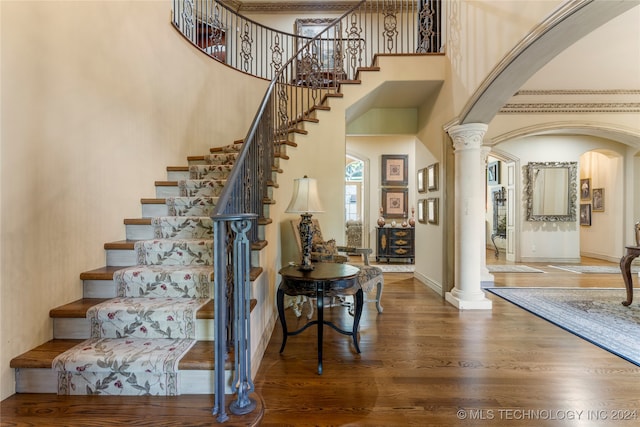 staircase with a high ceiling, hardwood / wood-style flooring, and decorative columns