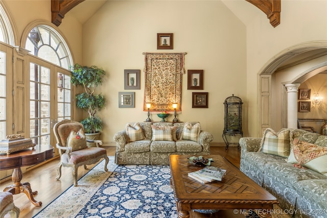 sitting room with high vaulted ceiling, ornate columns, wood-type flooring, beam ceiling, and french doors