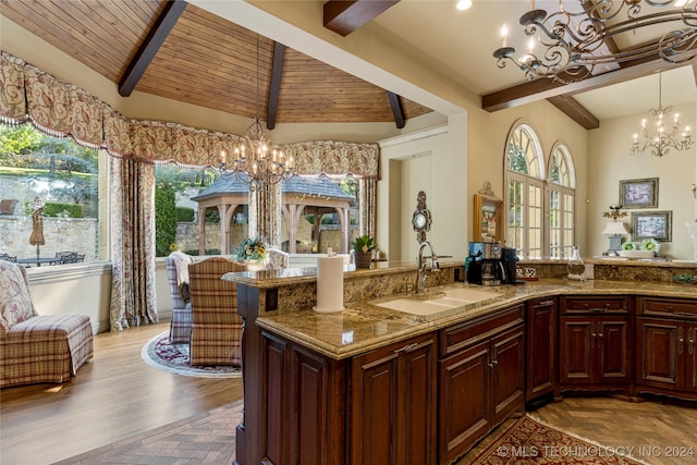 kitchen with vaulted ceiling with beams, sink, a notable chandelier, decorative light fixtures, and light stone counters