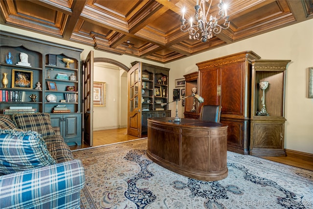 home office with light hardwood / wood-style floors, a notable chandelier, coffered ceiling, and ornamental molding