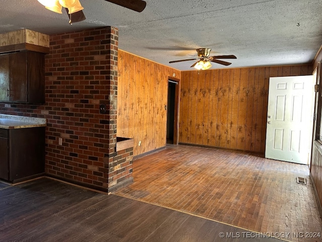 interior space with ceiling fan, dark hardwood / wood-style flooring, wood walls, and a textured ceiling