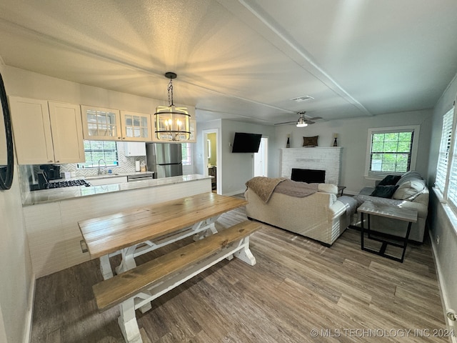 dining area featuring light hardwood / wood-style flooring, sink, ceiling fan with notable chandelier, and a brick fireplace