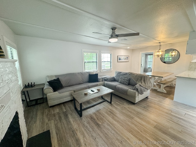 living room with a textured ceiling, hardwood / wood-style floors, ceiling fan with notable chandelier, and a fireplace