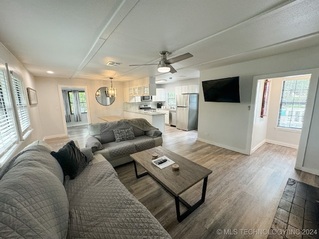 living room featuring a textured ceiling, ceiling fan with notable chandelier, and light wood-type flooring