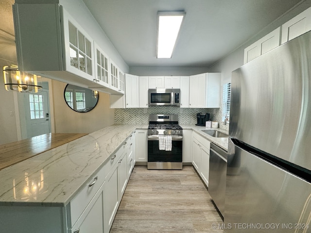 kitchen featuring stainless steel appliances, light stone counters, sink, white cabinets, and light hardwood / wood-style floors