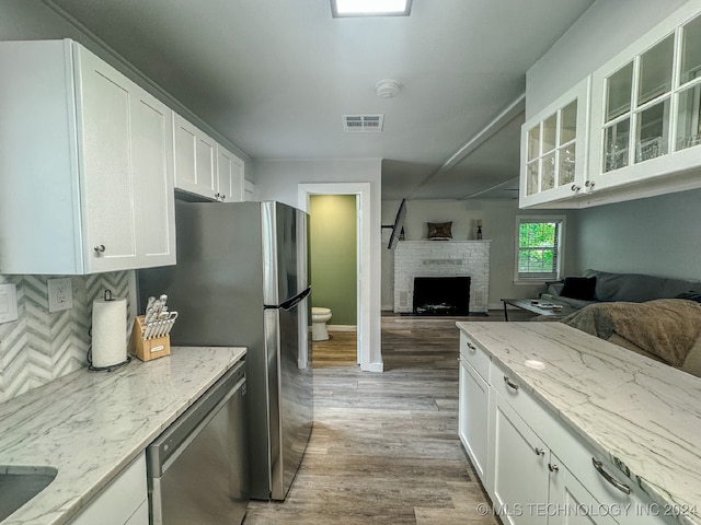 kitchen featuring white cabinets, hardwood / wood-style floors, light stone counters, and a brick fireplace