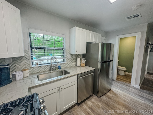 kitchen with white cabinets, stainless steel appliances, light hardwood / wood-style floors, sink, and tasteful backsplash