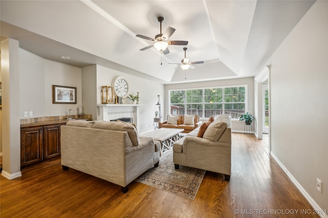 living room with a tray ceiling, ceiling fan, and dark wood-type flooring