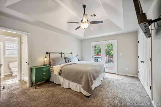 bedroom with french doors, access to outside, a tray ceiling, ceiling fan, and connected bathroom