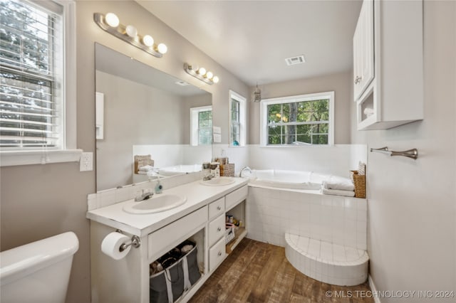 bathroom with tiled bath, toilet, hardwood / wood-style flooring, and vanity