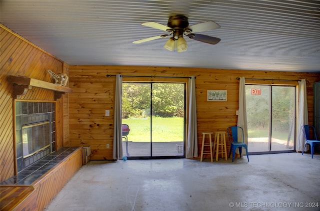 unfurnished living room with ceiling fan, concrete floors, a tile fireplace, and wooden walls