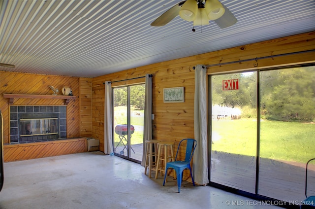 doorway featuring ceiling fan, a fireplace, wood walls, and concrete floors