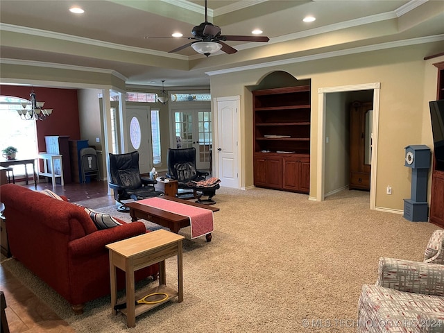 carpeted living room with ornamental molding, ceiling fan with notable chandelier, and a tray ceiling