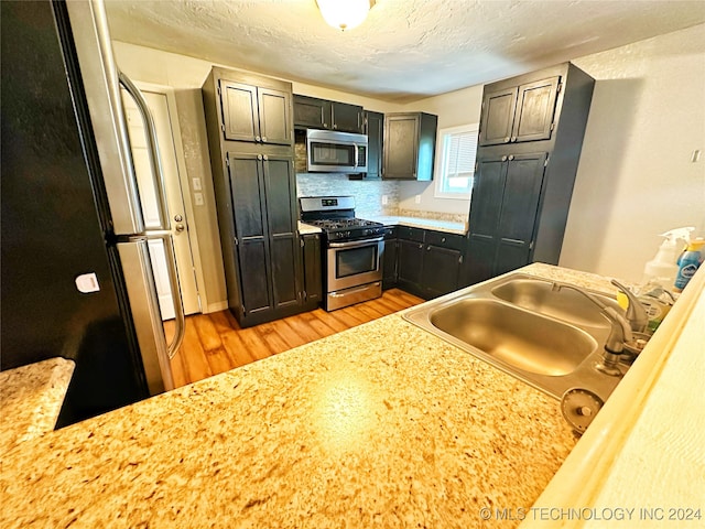 kitchen with appliances with stainless steel finishes, light hardwood / wood-style flooring, tasteful backsplash, sink, and a textured ceiling