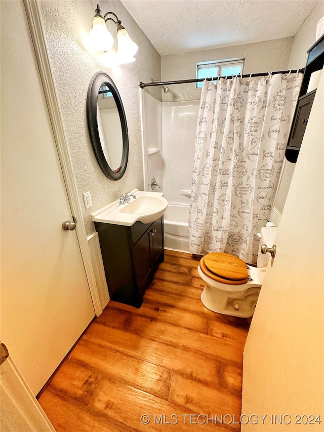 full bathroom featuring toilet, vanity, hardwood / wood-style floors, shower / tub combo, and a textured ceiling