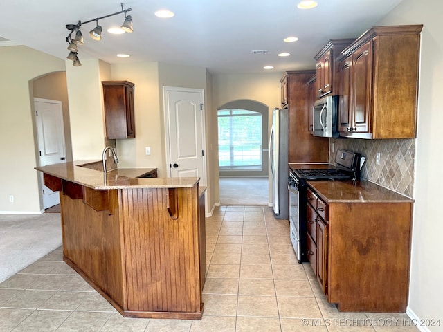 kitchen featuring appliances with stainless steel finishes, kitchen peninsula, decorative backsplash, and light carpet