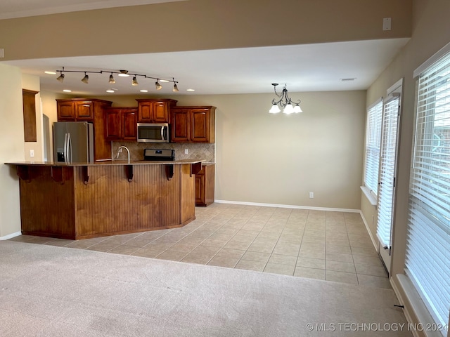 kitchen featuring a kitchen bar, an inviting chandelier, appliances with stainless steel finishes, decorative backsplash, and light carpet